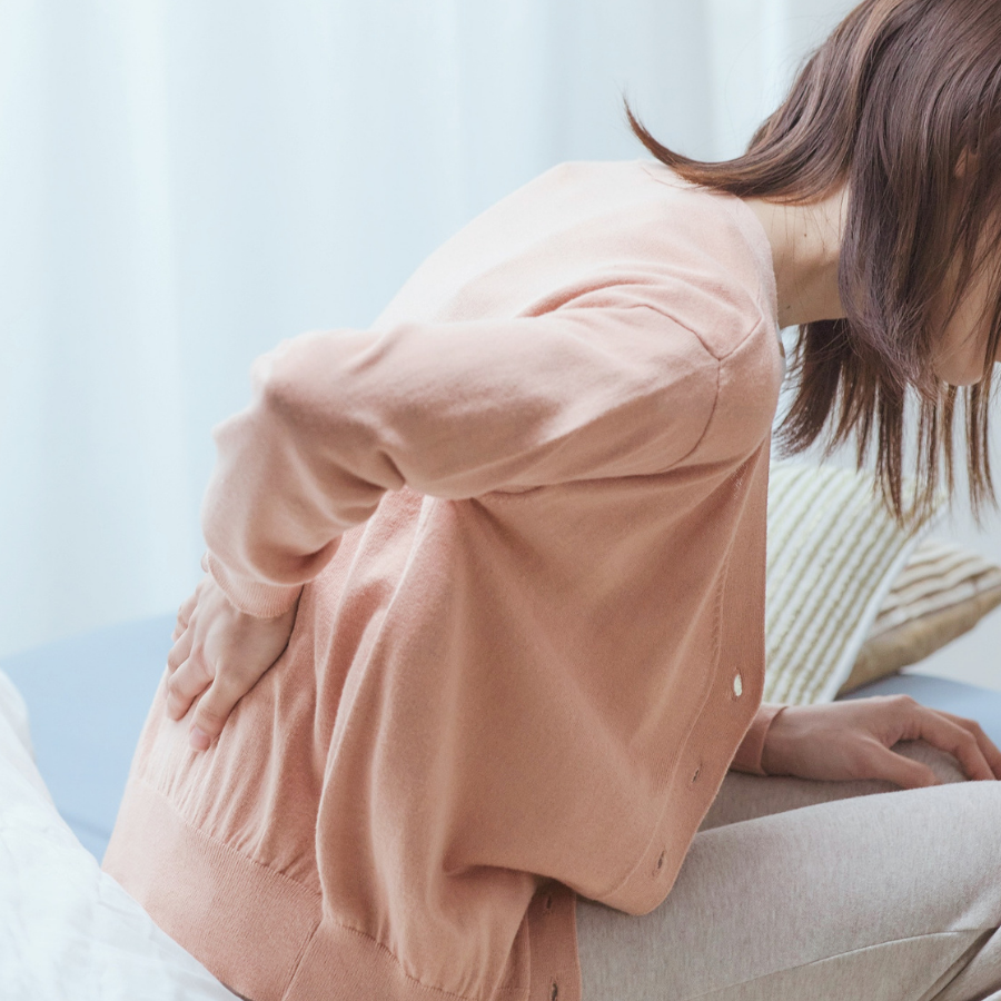 背中の張りや痛みを感じ、背中に手を当てている女性