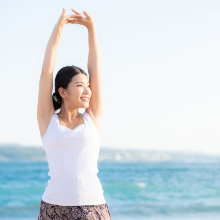 海辺で気持ちよく伸びをする女性の写真