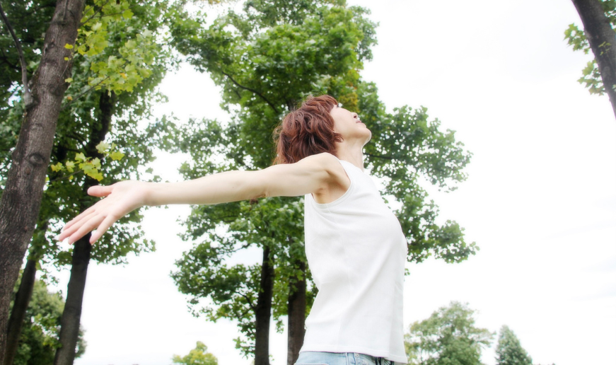 自然の中で、両手を広げて空を見上げるノリコの姿。体と丁寧に向き合い続けてきた歩みを象徴する一枚