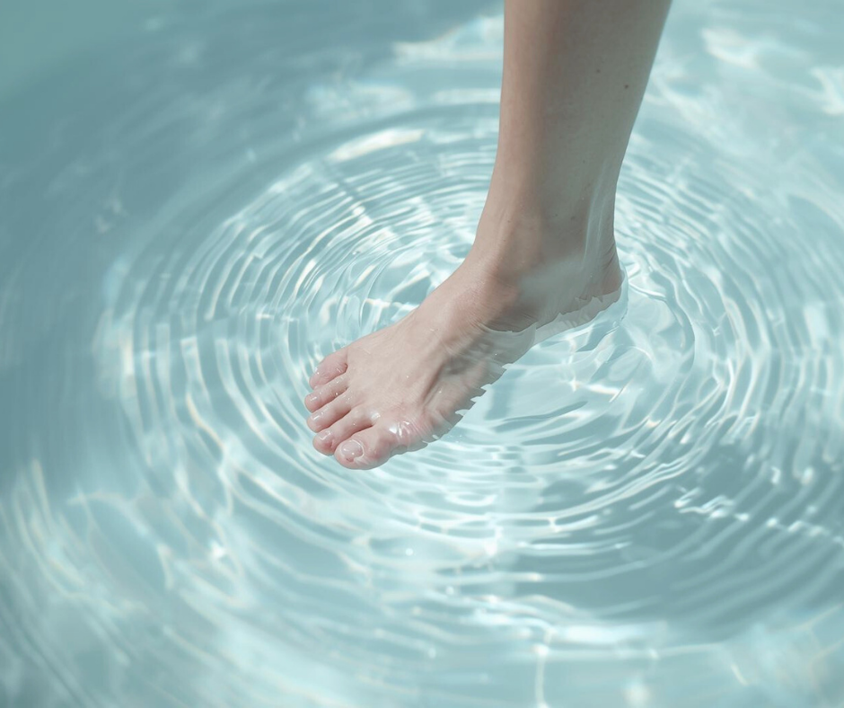 女性の素足が水面に触れ、柔らかな波紋が広がる様子