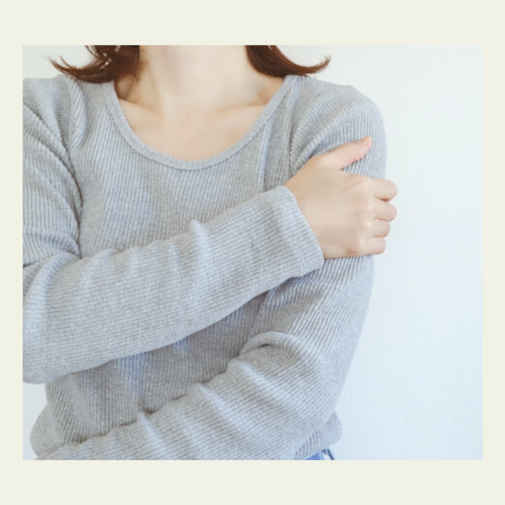 片方の腕を手で押さえる女性の動作