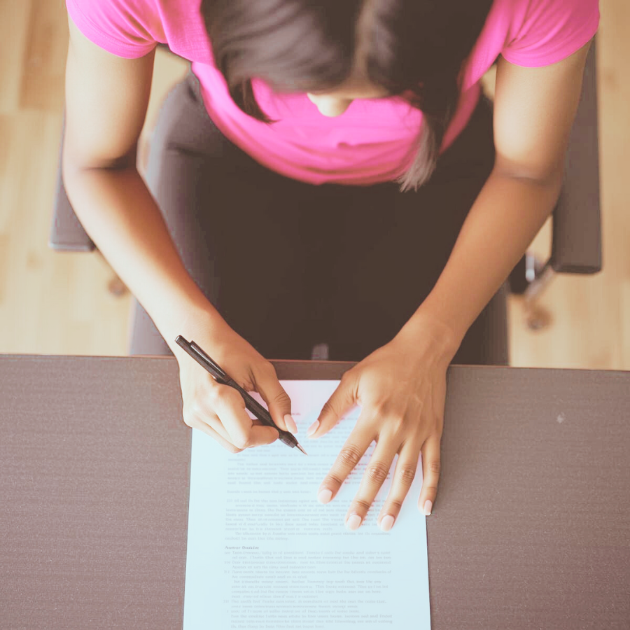 机に向かい、紙にメモを書き込みながらイメージを整理する女性