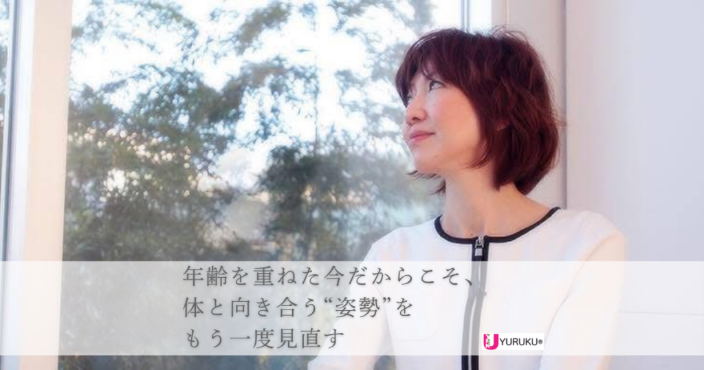 窓の外の木々と空を静かに眺めながら立つノリコ。体と丁寧に向き合う時間を象徴する一枚